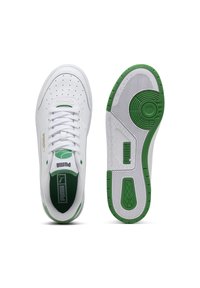 Hvide sneakers med grønne accenter, der har en perforeret læderoverdel, flade snørebånd og en tekstureret gummisål med cirkulære detaljer.