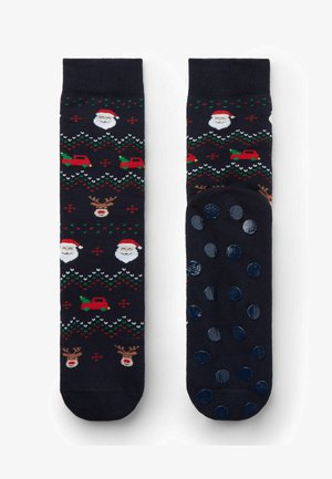 Schwarze Socken mit festlichen Motiven von Santa-Gesichtern, Rentieren und Weihnachtsbäumen in Rot und Grün. Texturiertes, gepunktetes Grip-Muster auf der Unterseite.