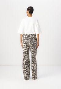 Beige og svart leopardmønstrede jeans med rette ben. Kombinert med en løs hvit T-skjorte, sett bakfra.