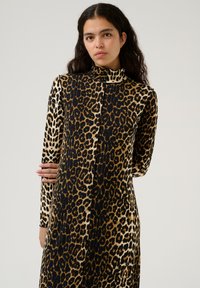 Vestido de manga larga con estampado de leopardo que presenta un cuello alto y un diseño sin costuras. Fabricado con un tejido suave que presenta distintivos patrones en negro y dorado.
