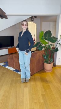 Mustaline ribatatud pikad varrukad, helesinised teksad, pruunid pahkluu saapad; mugav elutuba taime ja pruuni kalli džinsist diivaniga.