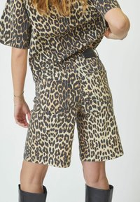 Traperice kratke hlače s leopard uzorkom, s dva stražnja džepa, poderanim rubom i crnim pojasom. Tekstura je mekana s izraženim životinjskim uzorcima.