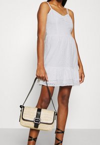 Vit klänning i ögla med spaghettiband och volangkant. Beige vävd handväska med svart rem och detaljer i metall.