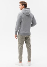 Felpa grigia con cappuccio regolabile, polsini e orlo a coste, abbinata a pantaloni jogging grigio chiaro con vita elastica e sneakers bianche.