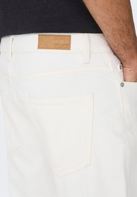 Jeans de mezclilla blanca con una etiqueta de cuero en la cinturilla. Se pueden ver costuras detalladas y dos bolsillos traseros.