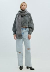 Grauer, gestrickter Cropped-Pullover mit langen Ballonärmeln, kombiniert mit hellblauen, ausgewaschenen Schlagjeans und einem passenden grauen Schal. Schwarze Stiefeletten mit Absatz.
