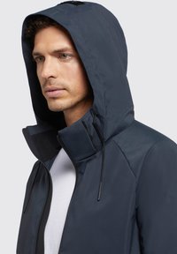 Chaqueta azul marino con capucha, hecha de tela suave. Cuenta con un cuello alto y cordones ajustables. Parte frontal con cremallera, detalles de diseño mínimos.