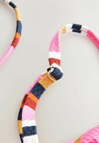 Bretelles en tissu coloré et rayé de rose, marine, orange et blanc avec un détail en anneau métallique doré reliant deux sections. Fini texturé.