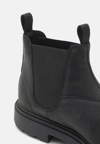 Bottines en cuir noir avec panneaux élastiques sur les côtés, tirant à l'arrière et semelle en caoutchouc texturée, au design minimaliste et aux détails de couture.