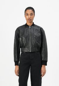 Must mustriga bomber-jakk, mis on valmistatud kunstnahast, omab ribaga kaelust, mansette ja vöökoht. Sulguve eesmine tõmblukk.