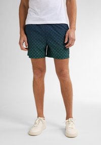 Pantaloni da nuoto blu navy con motivo di palme verdi, realizzati in tessuto leggero, con vita elastica e taglio rilassato.