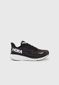 Scarpa da ginnastica nera con tomaia in rete traspirante, logo bianco, suola spessa e ammortizzata, e motivo a zigzag su un lato per una maggiore aderenza.