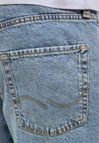 Light blue denim jeans back pocket with orange stitching, featuring a curved design pattern, and a textured fabric surface.