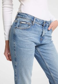 Jeans in denim azzurro chiaro con taglio dritto, caratterizzati da vita media, tasche frontali e dettagli di cucitura sottili. Etichetta semplice sulla cintura.