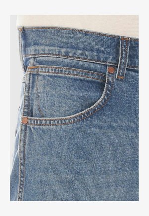 Light blue denim jeans featuring a standard five-pocket design, copper rivets, and contrasting orange stitching on the seams.