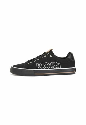 Czarny niski sneaker z czarnymi sznurowadłami, białym napisem „BOSS” po boku, gumową podeszwą z czarnymi i brązowymi paskami oraz skórzaną łatką na pięcie.