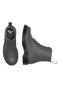 Botas de tobillo de cuero gris con una superficie texturizada, punta redonda y suela de goma negra con costuras amarillas y un tirador en el talón.