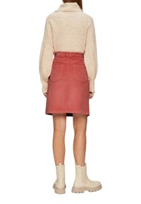 Pull beige tricoté court avec col montant, assorti à une jupe en velours côtelé rose avec poches arrière, porté avec des bottines épaisses beiges.