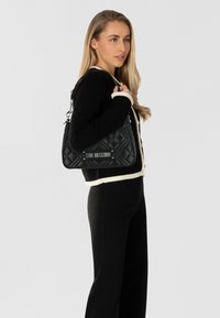 Schwarze, gesteppten Handtasche in dreieckiger Form, mit einem silbernen Logo-Plakette und einem abnehmbaren Umhängegurt. Strukturierte Oberfläche.
