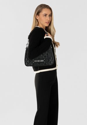 Schwarze, gesteppten Handtasche in dreieckiger Form, mit einem silbernen Logo-Plakette und einem abnehmbaren Umhängegurt. Strukturierte Oberfläche.