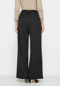 Zwarte brede broek met een hoge tailleband, gemaakt van een gladde stof en met een losse pasvorm, gecombineerd met zwarte hoge hakken.