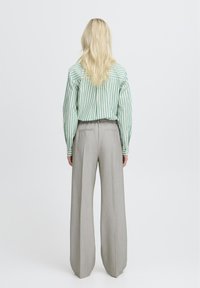 Camisa de manga larga a rayas verdes y blancas combinada con pantalones de pierna ancha en gris claro, con una textura suave y un ajuste entallado.