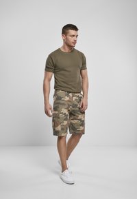 T-shirt verde oliva a maniche corte abbinato a pantaloni cargo camouflage con tasche laterali, vestibilità comoda e sneakers bianche.