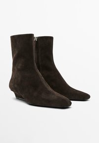 Braune Wildleder-Stiefeletten mit spitzer Kappe, ausgestattet mit einem seitlichen Reißverschluss und niedrigem Keilabsatz. Glatte Textur und saubere Nähte.