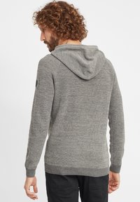 Szary dzianinowy hoodie z teksturowanym wzorem, ściągaczami przy mankietach i u dołu. Posiada dopasowany kaptur oraz małe logo na lewym rękawie.