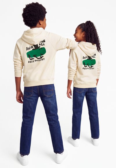 Deux enfants portant des sweat-shirts à capuche beiges avec un graphisme de lézard vert et le texte "Animals Observatory,", debout côte à côte, souriants.