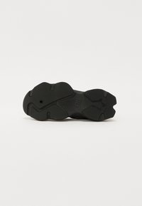 Svart såle til sneakers med teksturert grep, som har en buet form, avrundet hæl og et sentralt stjernesymbol. Designet for grep og holdbarhet.