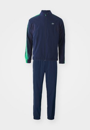 Chándal azul marino que incluye una chaqueta con cremallera y detalles en verde, combinada con pantalones ajustados a juego y detalle del logo.