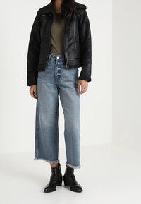 Czarna kurtka z ekoskóry z kołnierzem z baranka, oliwkowy top, jasnoniebieskie szerokie dżinsy z postrzępionym dołem oraz czarne botki sięgające kostki.