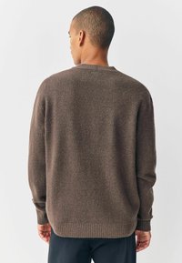 Brown knit sweater featuring a ribbed hem and cuffs, round neckline, and a relaxed fit, showcasing a soft, textured finish.