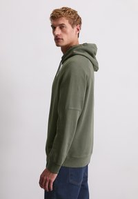 Sweat-shirt à capuche en vert olive, en mélange de coton, avec une poche kangourou et des poignets et un ourlet côtelés. Texture lisse, coupe décontractée.
