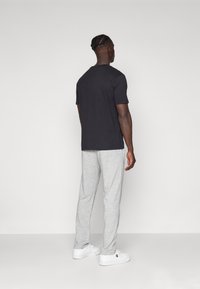 Schwarzes Kurzarm-T-Shirt kombiniert mit hellgrauen Jogginghosen, die einen lockeren Schnitt, eine glatte Textur und weiße Sneakers aufweisen.