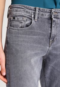 Šedé džíny z denimu s klasickým střihem, designem s pěti kapsami a jemným odřením. Viditelné švy a kovové detaily.
