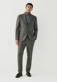 Gray houndstooth suit with a fitted jacket and straight-leg trousers, paired with a light gray turtleneck and black loafers. Smooth textures.