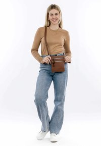 Borsa a tracolla in pelle marrone con tracolla regolabile, dotata di due tasche con zip e una texture liscia su uno sfondo neutro.