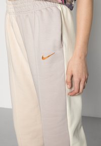 Nike trainingsbroek met een kleurblokdesign in crème, beige en lichtgrijs; elastische tailleband met zijzakken en een gouden logo-accent.