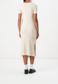 Robe midi en tricot côtelé beige avec manches courtes, fente latérale, coupe ajustée. Portée avec des chaussures noires et des chaussettes blanches à bords festonnés.