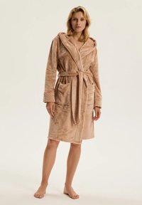 Beżowy pluszowy szlafrok z kapturem, wiązany w pasie i z dwoma przednimi kieszeniami. Charakteryzuje się miękką fakturą i długością do kolan.