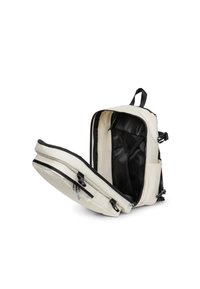 Pleciony plecak w kolorze kremowym z czarnym wnętrzem, całkowicie rozpięty, aby pokazać główną komorę, boczną kieszeń i regulowane paski na białym tle.