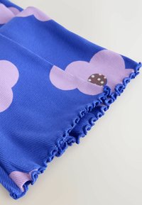 Tessuto blu con motivi di nuvole rosa, caratterizzato da un bordo arricciato. La trama è a costine e presenta un dettaglio a cerchio marrone con puntini bianchi.