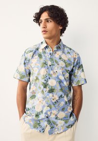 Kortærmet skjorte med knapper i lyseblåt stof med et blomsterprint med hvide blomster og grønne blade. Glat tekstur, afslappet pasform.