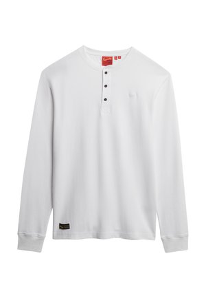 T-shirt henley blanc à manches longues avec trois boutons noirs, col rond et petite étiquette de marque noire près de l'ourlet.
