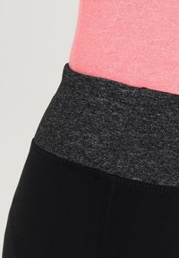 Mustat leggingsit, joissa on leveä harmaa vyötäröhihna teksturoidulla kuviolla, yhdistettynä sileään vaaleanpunaiseen yläosaan, joka näkyy vyötäröllä.