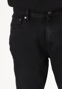 Svart denimjeans med en klassisk femlomme-design, med sølvhardware og en jevn tekstur. Stoffet virker solidt og figursydd.