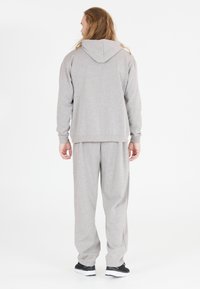 Grau Hoodie und passende Jogginghose, hergestellt aus weichem Stoff. Kapuzen-Design; lockere Passform; Bündchen an Handgelenken und Knöcheln. Schwarze Sport Schuhe getragen.