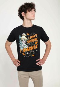 Camiseta negra con un gráfico de un personaje con cabello rubio y el texto "NO HAGO PÁNICO, BRILLO" en naranja, sobre un fondo colorido y texturizado.